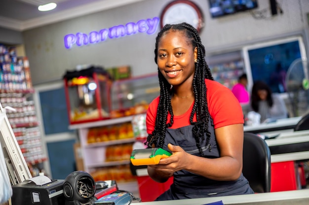 Vistas laterais da jovem caixa feminina segurando o terminal pos sorrindo olhando para a câmera esperando o cliente colocar