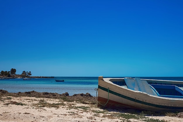 Vistas maravilhosas da costa do Mediterrâneo com praia de areia branca e um barco de pesca na Ilha de Djerba, Tunísia