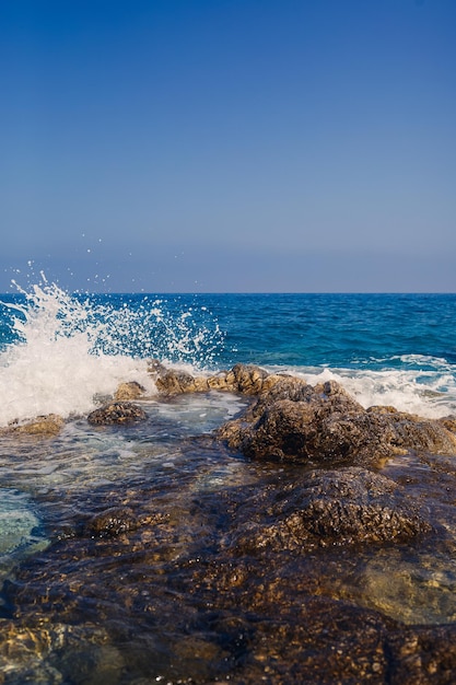 Vistas maravilhosas do mar Mediterrâneo azul Sunny balança as ondas com espuma e salpicos de água A onda bate nas rochas na costa