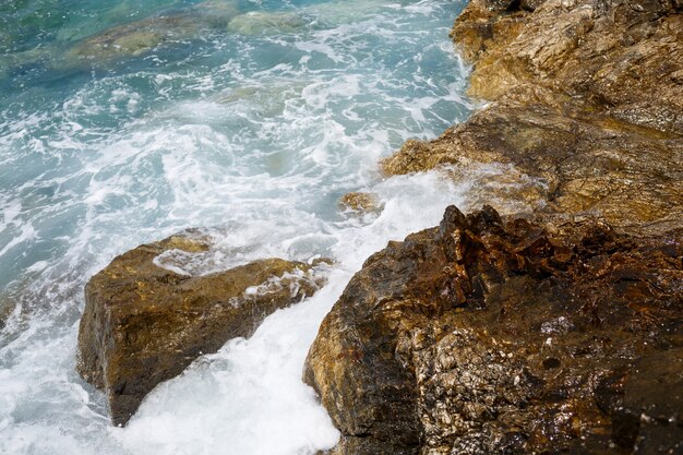 Vistas maravilhosas sobre o azul do Mar Mediterrâneo. Pedras ensolaradas, ondas com espuma e respingos de água. A onda bate nas rochas da costa