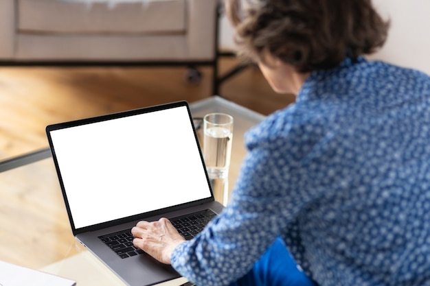 Vistas desde la parte posterior de la mujer de negocios de edad trabajando mientras usa una computadora portátil con pantalla en blanco