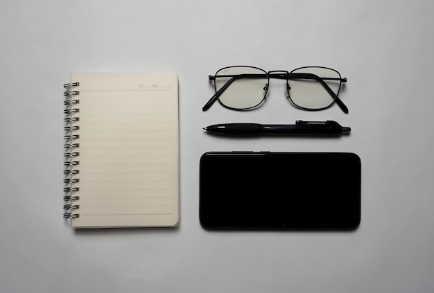 Visto de cima há um notebook com óculos de caneta e um smartphone