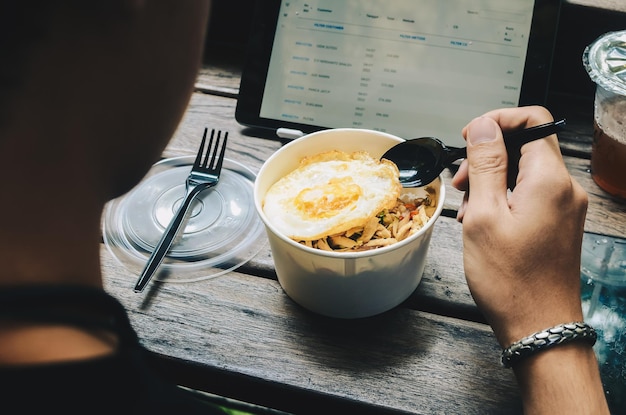 Visto desde detrás de un hombre asiático desayunando con un tazón de arroz con huevo