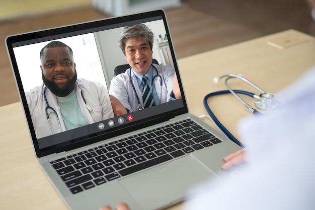 Visualização do aplicativo de tela de médico sênior asiático e afro-americano usando estetoscópio de jaleco branco no pescoço e videoconferência para discussão e compartilhamento de como curar o vírus. Conceito de telemedicina
