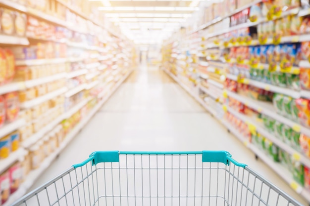 Visualização do carrinho de compras no corredor do supermercado com prateleiras de produtos, borrão abstrato e fundo desfocado