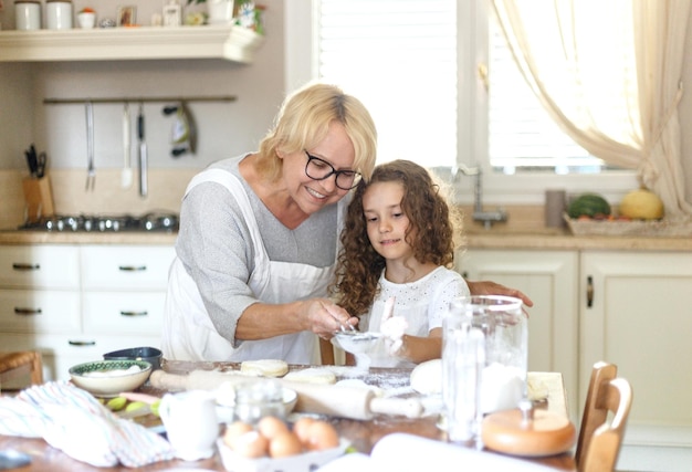 Visualização horizontal. Uma avó e uma sobrinha estão cozinhando. Uma avó sorridente está cozinhando biscoitos. Fique em casa e cozinhe com seus entes queridos.