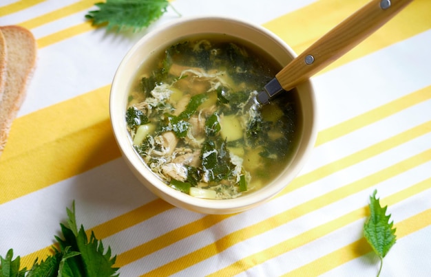 Vitamin-Brennnesselsuppe hellgelber Hintergrund und grüne Brennnesseln auf der Tischplatte anzeigen Gesunde Sommersuppe