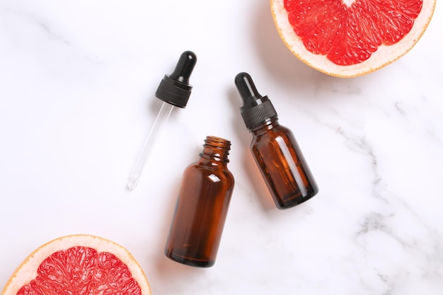 Vitamin-C-Gesichtskosmetik dunkle Flaschen mit Tropfen roten Grapefruitscheiben auf Marmorhintergrund