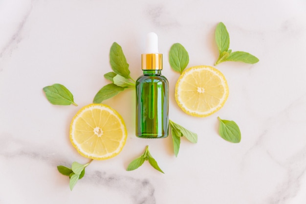 Vitamin C-Serum in Kosmetikflasche mit Zitronen-Zitrusscheiben mit grünen Blättern auf Marmoroberfläche
