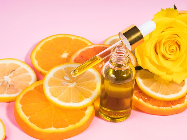 Vitamin-C-Serumflasche mit Tropfer auf rosafarbenem Hintergrund mit orangefarbenen Zitrusscheiben