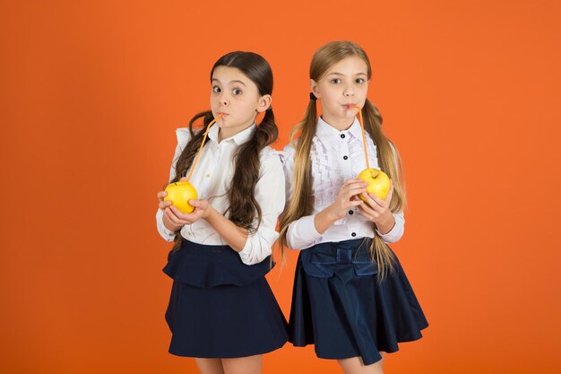 Vitamin-Ernährung während des Schultages Steigern Sie die Akzeptanz von Obst durch die Schüler Verteilen Sie kostenlos frisches Obst in der Schule Mädchen Kinder Schuluniform orange Hintergrund Schulmädchen essen Äpfel Schulessen