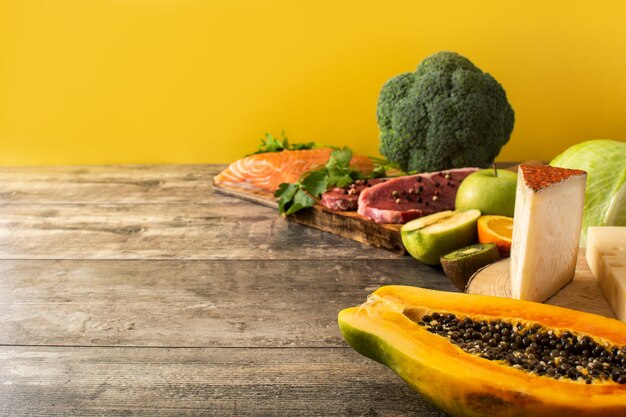 La vitamina A en los alimentos con frutas, verduras, queso, pescado y carne en la mesa de madera y fondo amarillo