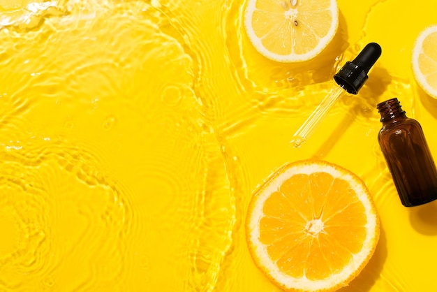 Vitamina C de soro de produto de garrafa cosmética com laranja e limão deitado sobre fundo amarelo limpo