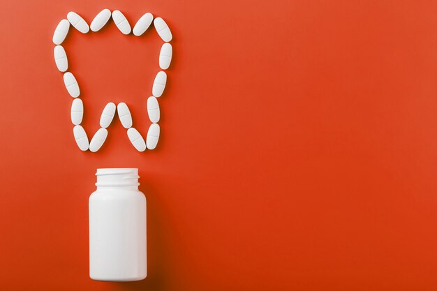 Vitamina de cálcio na forma de um dente derramado de um frasco branco sobre um vermelho.