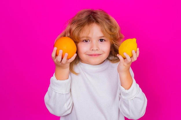 Vitamina y frutas saludables para niños Niño con naranja y limón en estudio Retrato de estudio de niño lindo sostener limón y naranja aislado sobre fondo rosa