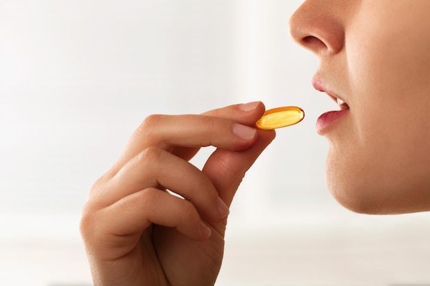 Vitamina y suplemento. Primer plano de una mujer joven hermosa que toma la píldora de aceite de pescado amarillo.