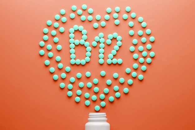 Vitaminas B 12 en forma de corazón sobre un sustrato rojo, vertidas en un frasco blanco.