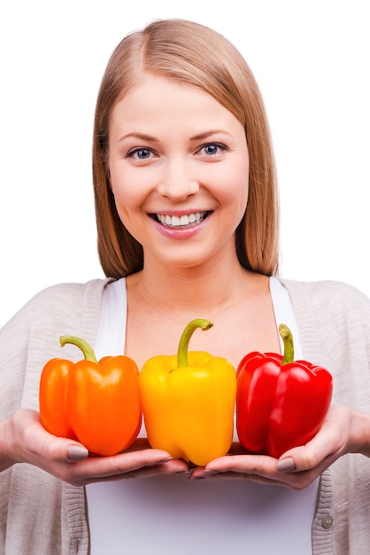 Vitaminas de colores. Hermosa mujer joven sosteniendo pimientos y mirando a la cámara mientras está de pie contra el fondo blanco.