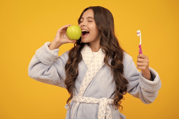 Vitaminas de manzana para dientes sanos Retrato de una adolescente caucásica sostiene un cepillo de dientes cepillándose los dientes higiene dental de rutina matutina aislada en el fondo amarillo