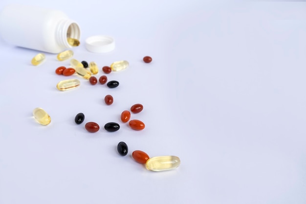 Vitaminas y suplementos para la salud junto a un frasco de plástico sobre fondo blanco.