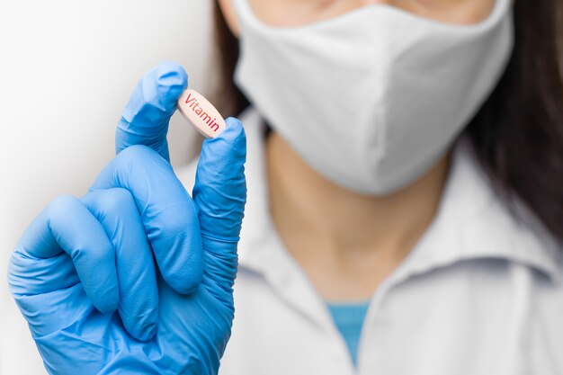 Vitaminpille in der Hand in blauen Handschuhen. Frau hält eine Medizin. Medikamente gegen Coronavirus, Ausbruch 2019-nCoV, SARS-nCov, COVID-2019.