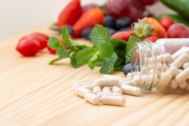 Foto vitaminpräparate in der glasflasche auf dem holztisch mit verschiedenen früchten