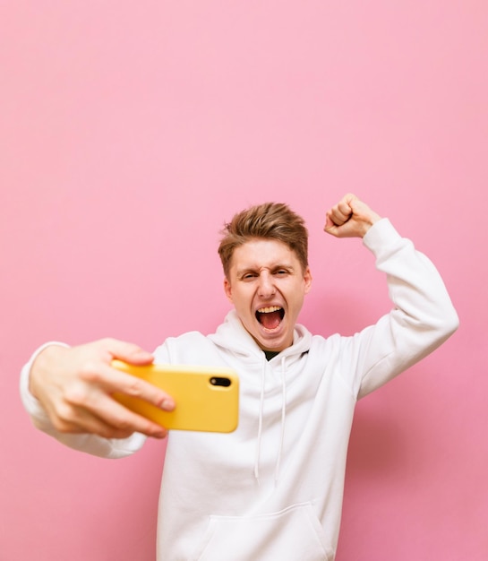 Vitória alegre do jogador emocional no jogo para celular com smartphone na mão isolado no fundo rosa