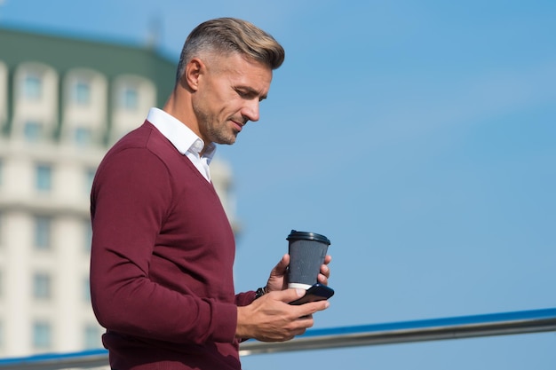 Vivendo o estilo de vida móvel homem bonito usa celular ao ar livre bebida matinal café para viagem tecnologia móvel 4g 3g comunicação empresarial marketing móvel chamada de vídeo vida moderna
