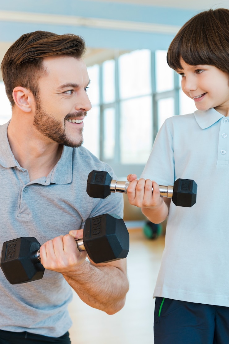 Foto vivendo uma vida saudável. pai e filho felizes se exercitando com halteres enquanto estão juntos na academia