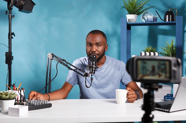 Vlogger afroamericano usando consola de control de volumen y grabando video con cámara profesional. Blogger creando contenido digital para el canal de medios sociales en estudio