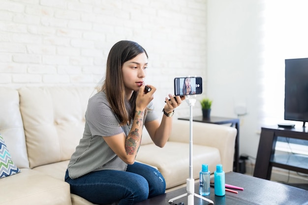 Vlogger aplicando lápiz labial mientras graba un video tutorial de maquillaje en casa