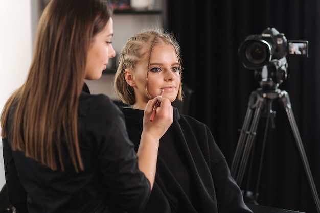 Vlogger de beleza de mulher bonita fazendo demonstração de maquiagem cosmética com uma amiga no estúdio