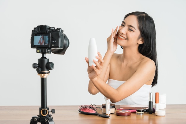 Vlogger de beleza profissional para jovem bela mulher asiática ou blogueiro gravando tutorial de maquiagem para compartilhar nas redes sociais sobre uma parede branca