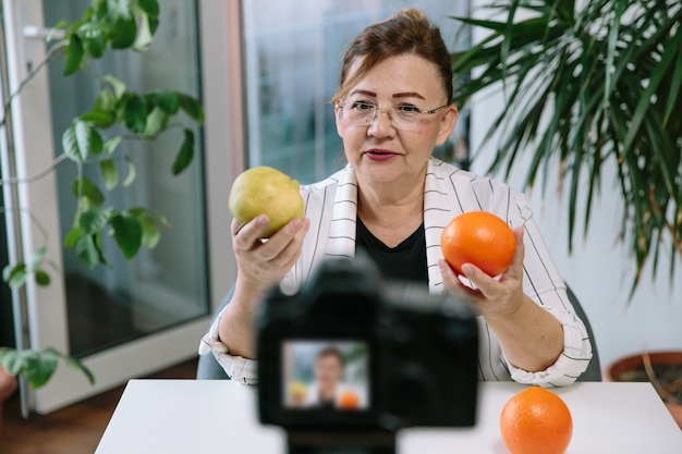 Vlogger de comida de mulher sênior gravando vídeo sobre alimentação saudável. mulher idosa, blogueira de estilo de vida, prepara novo vídeo para seu canal e se comunica com os seguidores.