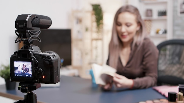 Vlogger haciendo una reseña de un libro frente a la cámara en su estudio creativo. Enfoque selectivo en la cámara