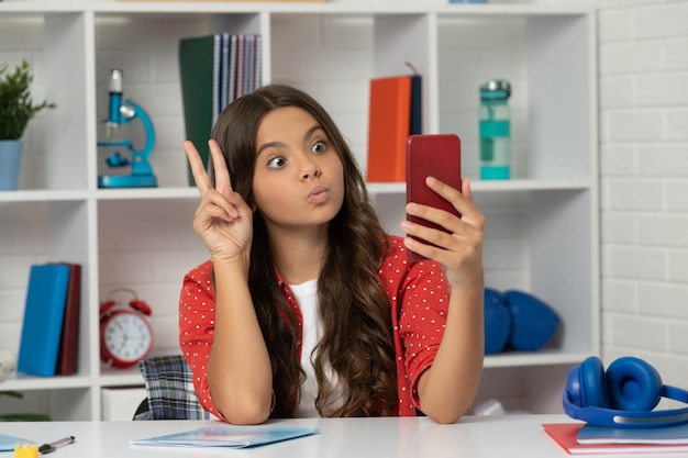 Vlogger mit handy zeigen friedensgeste glückliche jugendliche bloggerin benutzt smartphone zurück zur schule kind macht selfie im klassenzimmer 1. september kind macht videoblog bloggen am telefon