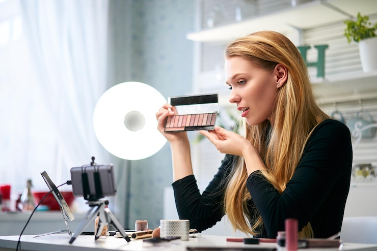 Foto vlogger mujer mostrando la paleta de sombras de ojos belleza blogger mujer filmando rutina de maquillaje diario tutorial cerca de la cámara en el trípode influencer chica transmisión en vivo de revisión de productos cosméticos en el estudio en casa