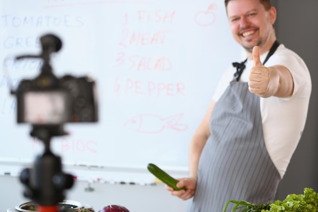 Vlogger riéndose sosteniendo un pene de pepino y filmando un video en la cámara