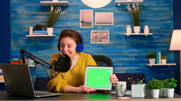 Vlogger schaut auf Laptop und spricht über Tablet mit Chroma-Key-Desktop