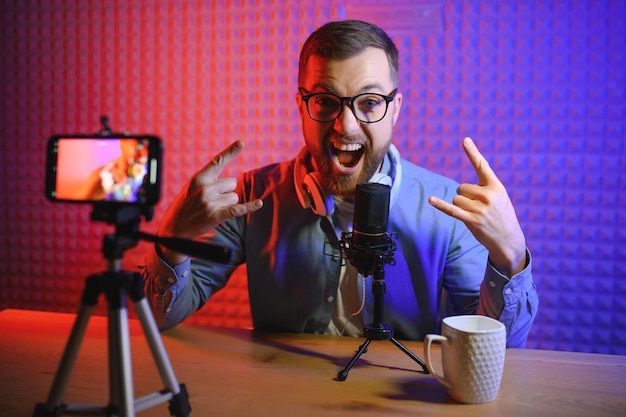Vlogger usando smartphone para filmar podcast em estúdio blogger com microfone de celular e fones de ouvido filmando vídeo para carreira de transmissão de mídia social