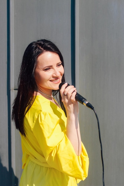 Vocalista feminina com cabelo escuro em um vestido segura um microfone nas mãos