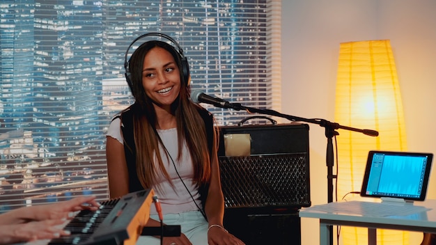 Vocalista negra sorridente no fone de ouvido cantando música no microfone no estúdio de gravação caseiro enquanto ela ...