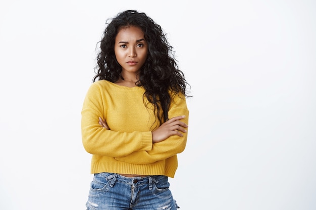 Você está fora do meu alcance. Atrevida, confiante, atraente, jovem mulher de cabelo encaracolado em uma camiseta amarela com os braços cruzados e levantando uma sobrancelha, olhar impressionado, expressar desdém e descrença