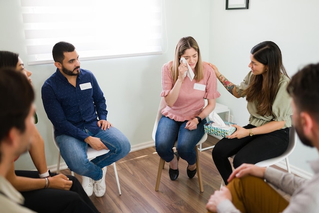 Você vai ficar bem. mulher jovem e atraente se sentindo deprimida e chorando em uma reunião de aconselhamento. membro do grupo de apoio confortando uma mulher triste com dependência de álcool