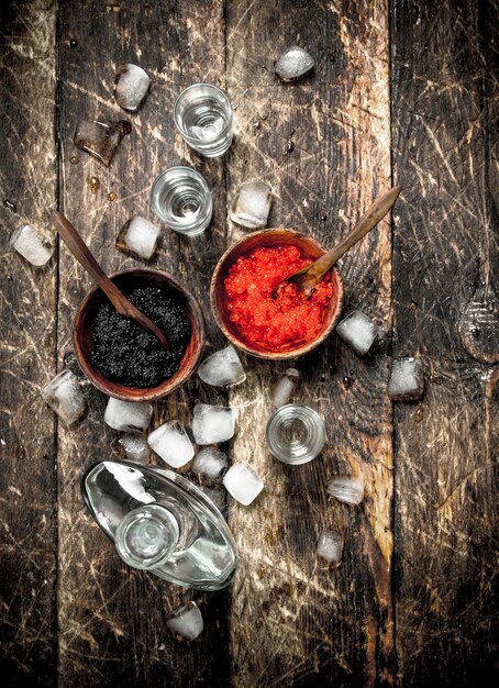 Vodka en botella con caviar negro y rojo. Sobre fondo de madera.