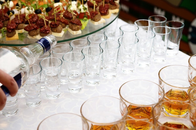 Vodka derrama de uma garrafa em um tiro em pé sobre a mesa branca