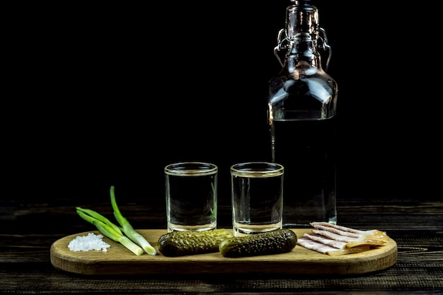 Foto vodka y dos vasos y pepinos con tocino y cebolla.