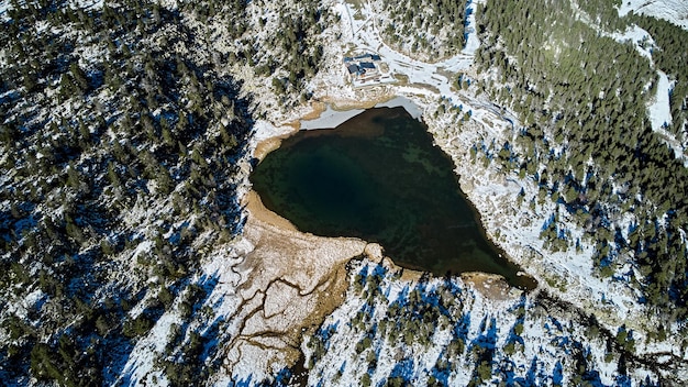 Vogelperspektive auf einen See inmitten der Berge, umgeben von Schnee im Winter