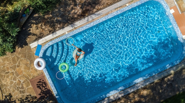 Vogelperspektive des schönen Mädchens im Swimmingpool von oben, schwimmen auf aufblasbarem Ringdonut und hat Spaß im Wasser auf Familienurlaub auf tropischem Ferienort