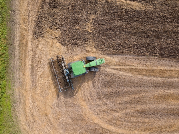 Vogelperspektive von der Drohne des Feldes nach der Ernte. Der Traktor pflügt das Feld und bereitet den Boden für landwirtschaftliche Arbeiten vor. Draufsicht